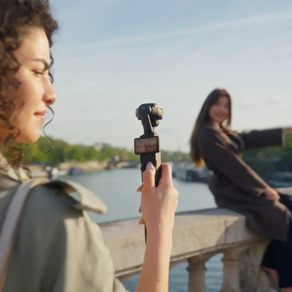 DJI Osmo Pocket 4P Dual-Camera Pocket Gimbal, 1-Inch Sensor, 60mm 3x Zoom, bkack, Person holding a camera stabilizer with another person in the background by a river